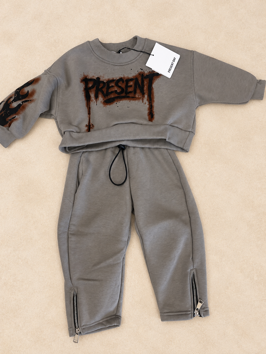 Completo tuta tortora Present Day da ragazzo, composto da felpa girocollo con stampa grafica e pantalone lungo con coulisse e zip alle caviglie.