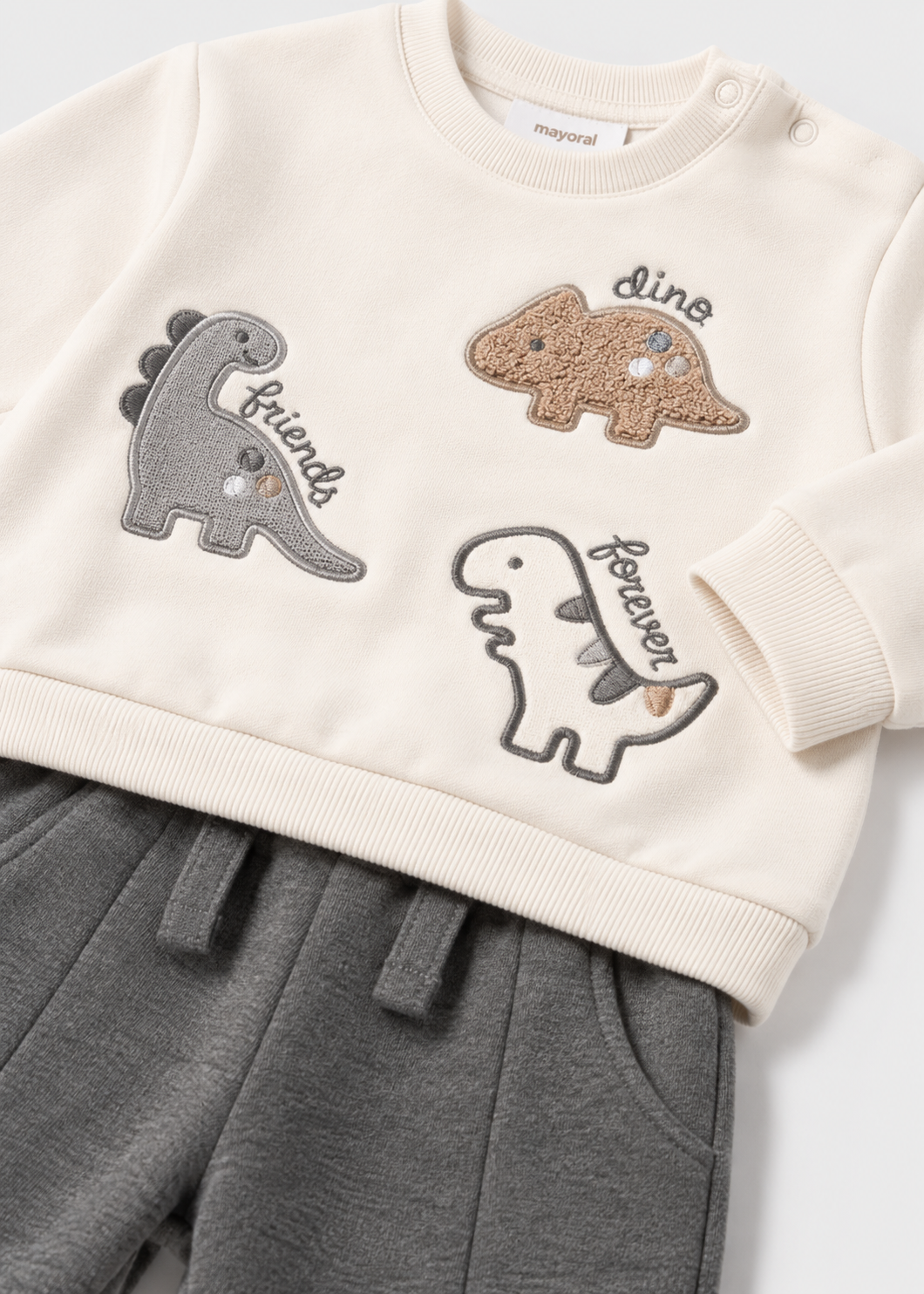 Dettaglio felpa neonato Mayoral écru con applicazioni di dinosauri e pantalone jogger grigio